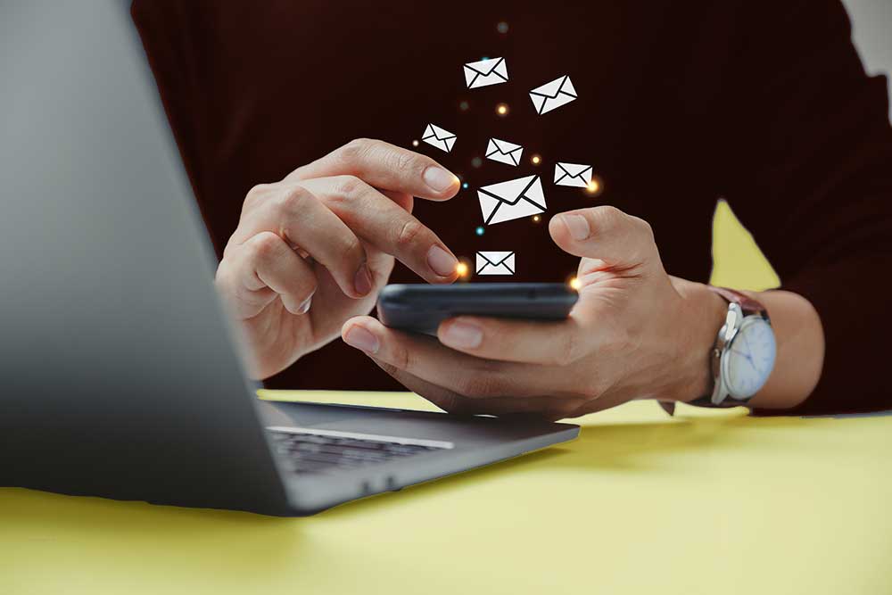 SEt up your personal email through gmail photo of person at computer with phone, email icons emitting from phone